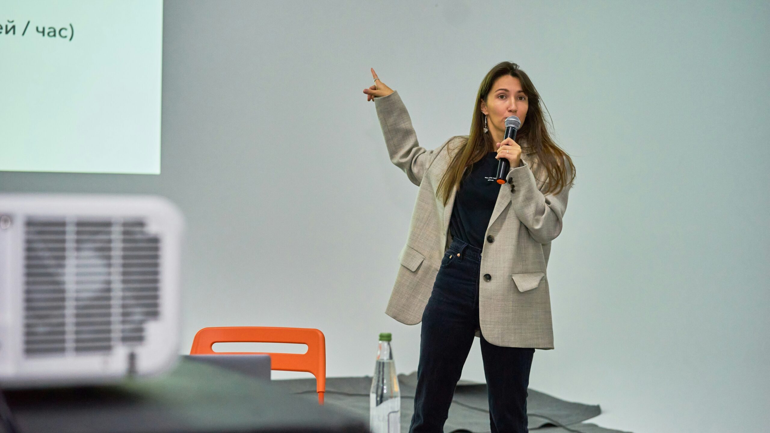 Mlada žena drži mikrofon i pokazuje na prezentacijski ekran tijekom izlaganja