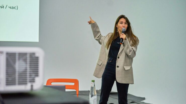 Mlada žena drži mikrofon i pokazuje na prezentacijski ekran tijekom izlaganja