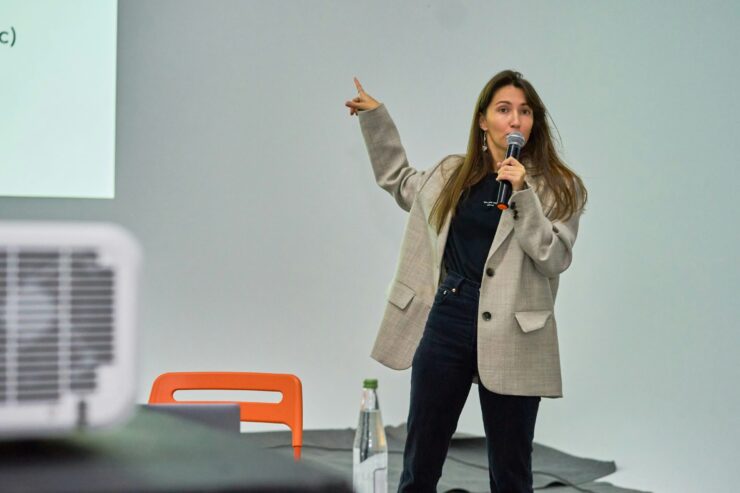 Mlada žena drži mikrofon i pokazuje na prezentacijski ekran tijekom izlaganja